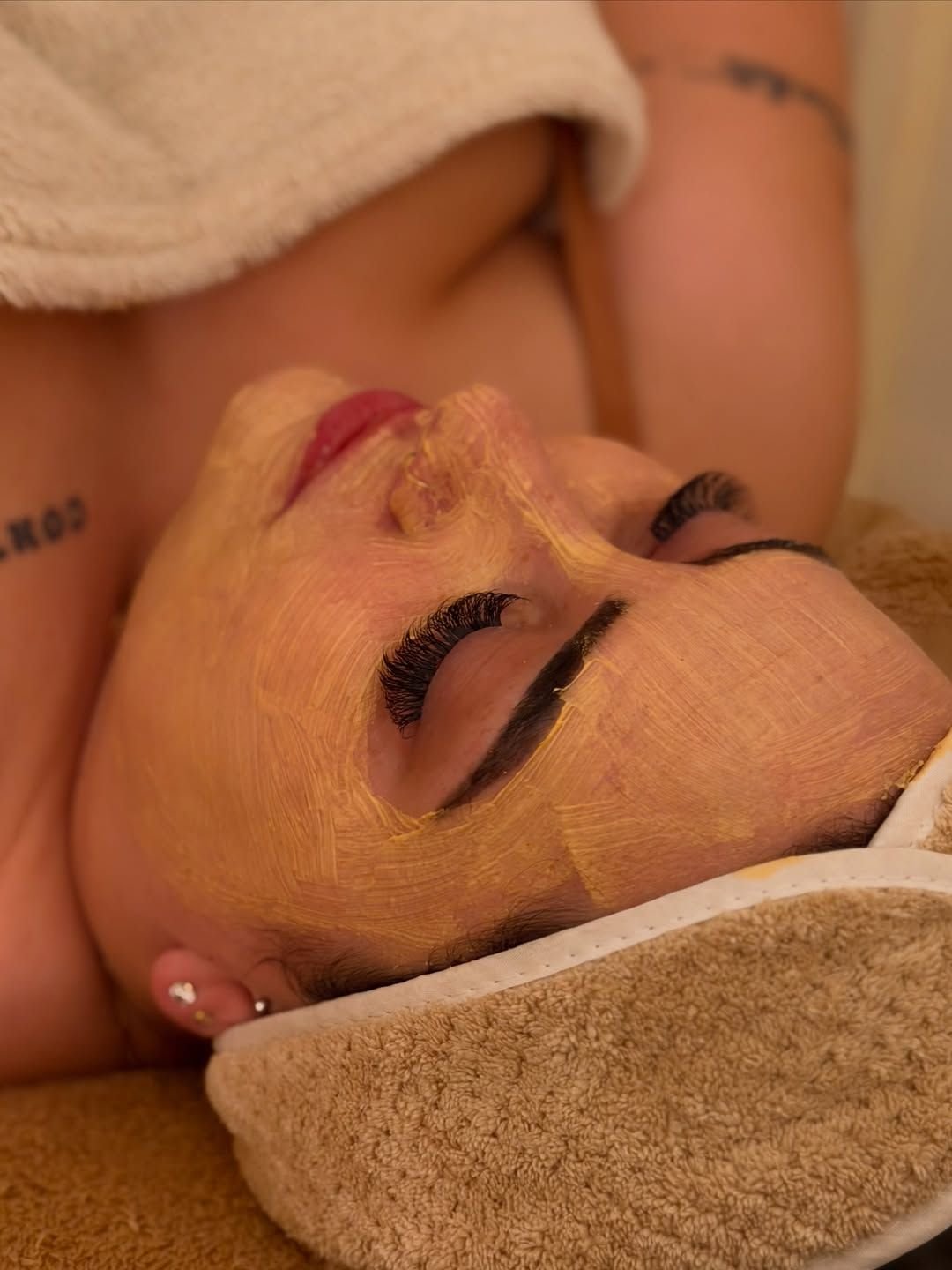 Paciente relaxada com máscara facial dourada durante protocolo de cuidado com a pele